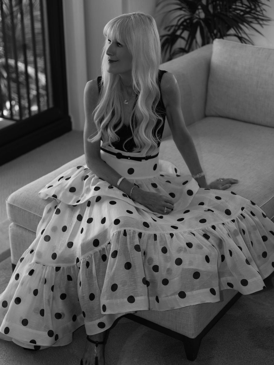 Woman wearing a sleeveless black top with a sheer polka dot skirt, seated on a sofa indoora