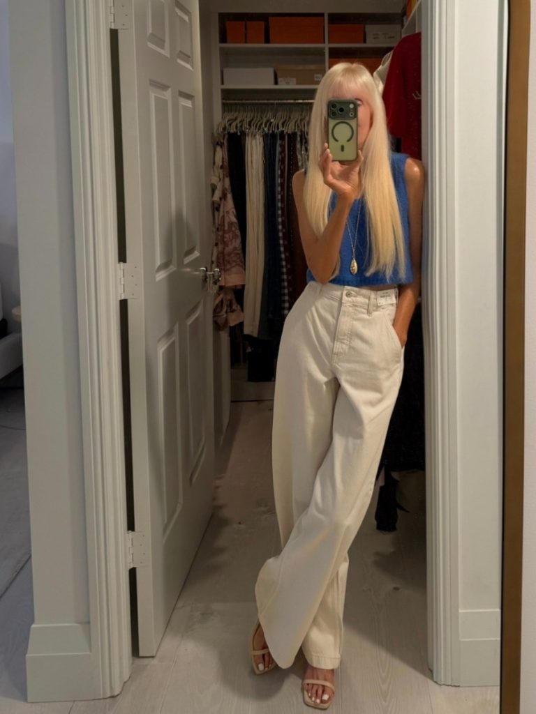 Mary wearing a modern classic summer outfit with high-waisted wide leg cream pants, a cropped blue knit top, and neutral sandals, styled with clean lines and effortless proportions.