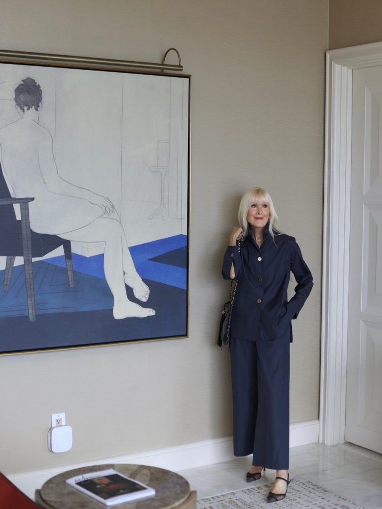 Woman wearing a navy matching set with a button-front top and wide-leg trousers styled with black slingback heels and a quilted handbag in a modern, elegant interior.