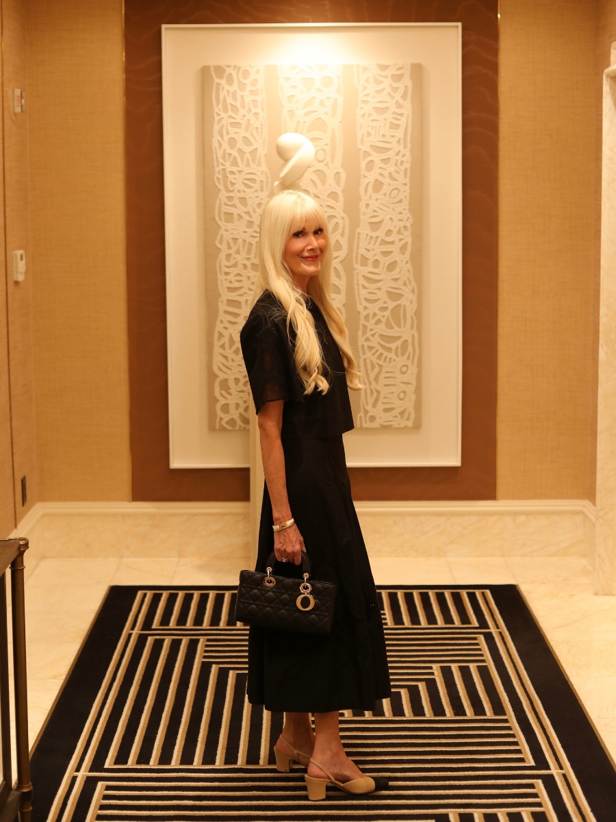 Woman wearing a black matching set with two-tone slingback heels and a structured black handbag in a sophisticated hotel interior.