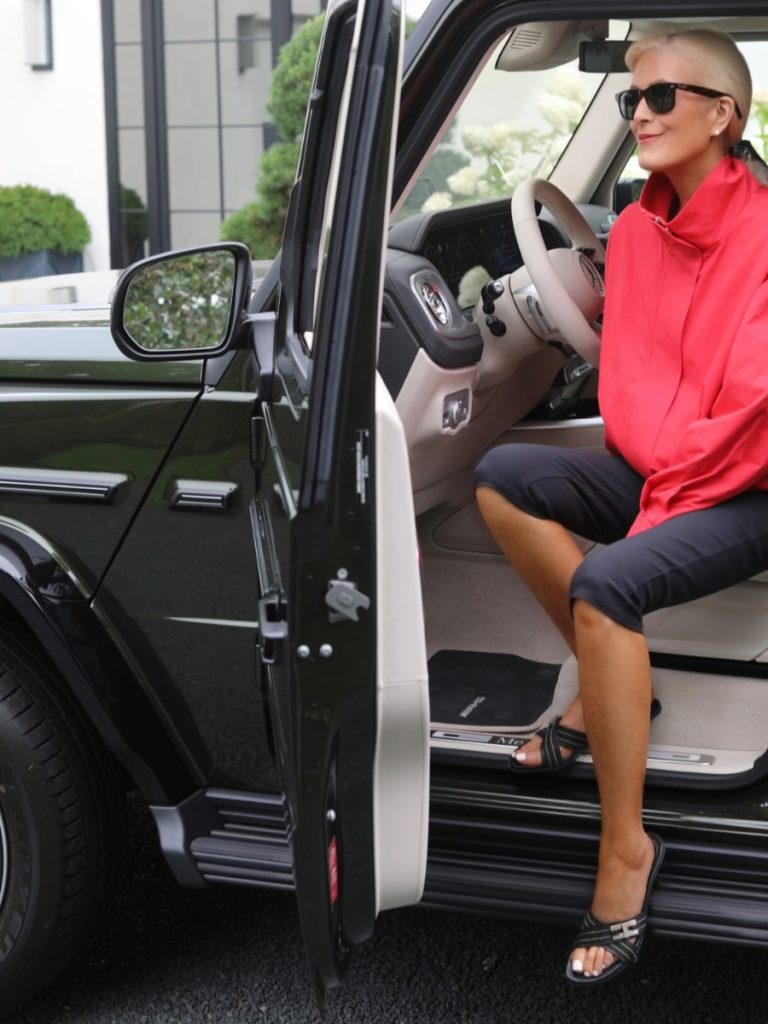 Woman wearing black capri pants with a bright red jacket, black sandals and sunglasses for a polished summer outfit.