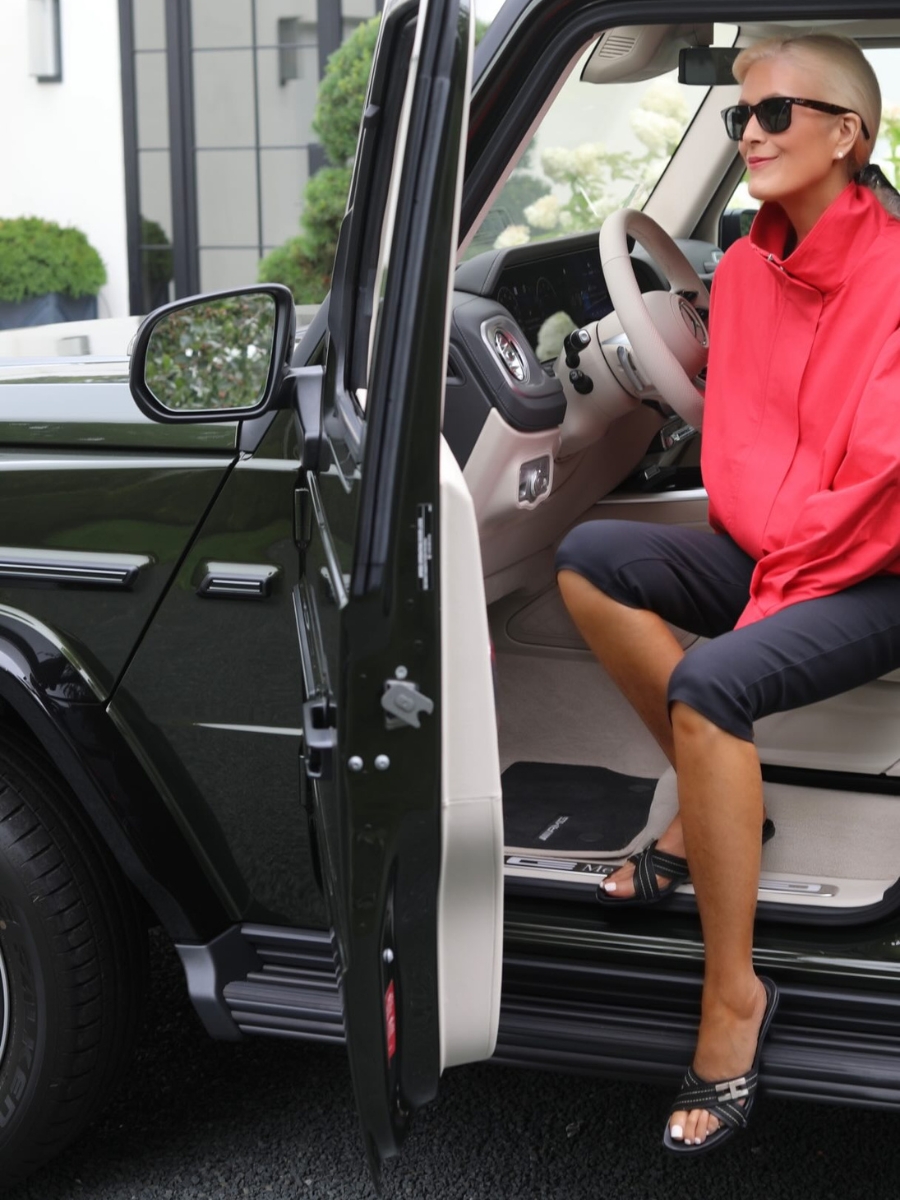 Woman wearing black capri pants with a bright red jacket, black sandals and sunglasses for a polished summer outfit.