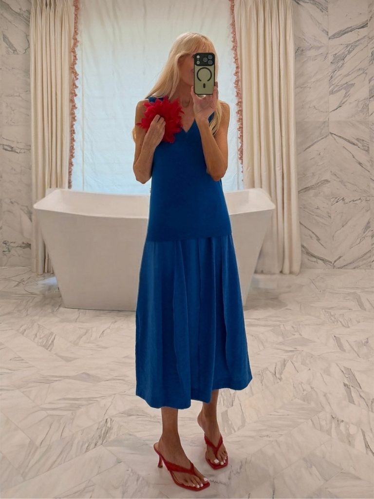 Mary wearing a cobalt blue Theory top and midi skirt with red Britt Netta heels and a red feather brooch