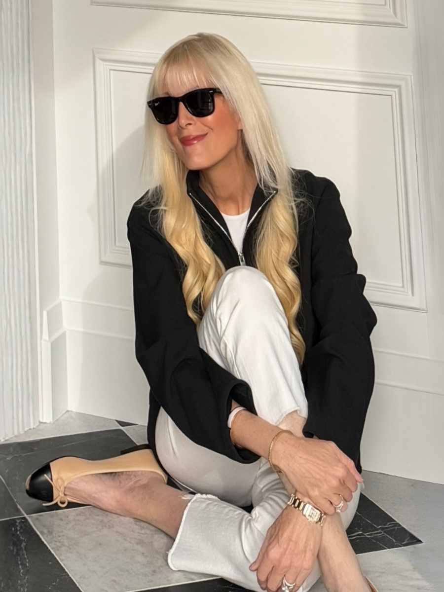 Mary Murnane wearing white jeans with a black zip-front jacket, white tee, beige heels with black cap toes, black sunglasses and gold jewelry.